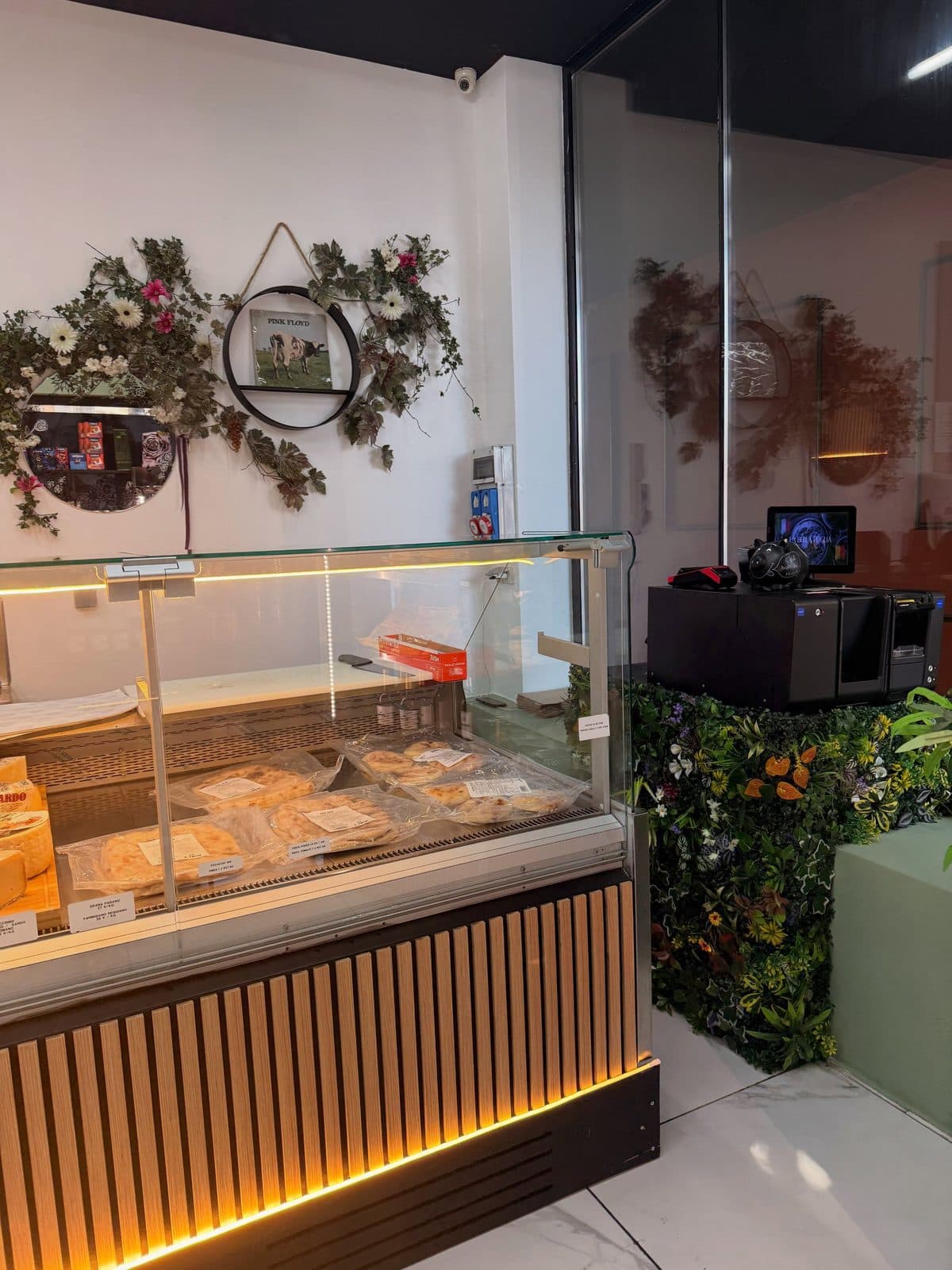 Le comptoir de caisse et sa vitrine, une couronne de fleurs au mur et le mur végétal à droite